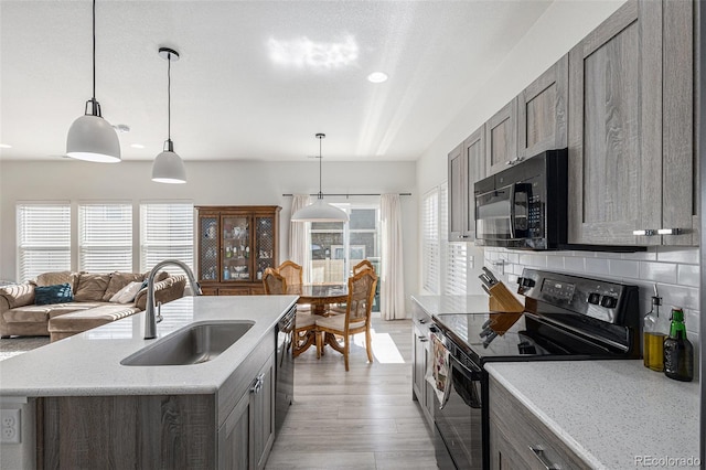 kitchen with decorative backsplash, light hardwood / wood-style flooring, sink, black appliances, and decorative light fixtures