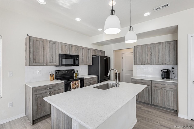 kitchen featuring a center island with sink, black appliances, light hardwood / wood-style floors, decorative light fixtures, and sink