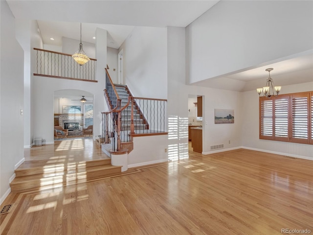 unfurnished living room featuring light wood-type flooring, a high ceiling, and ceiling fan with notable chandelier