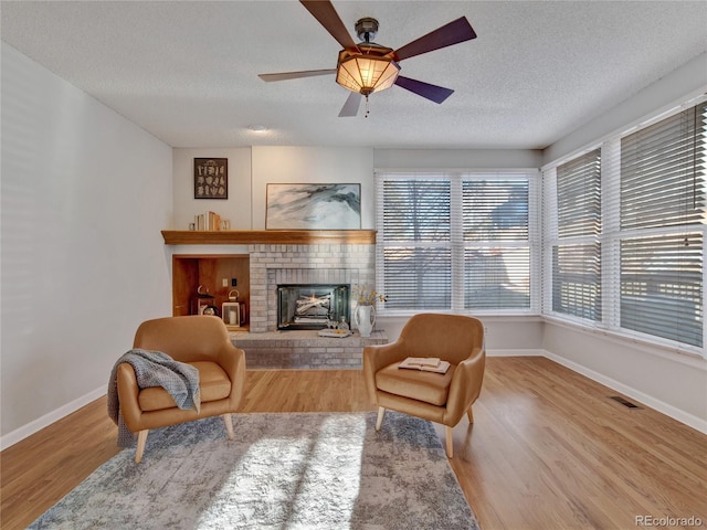 sitting room with wood-type flooring, a textured ceiling, a brick fireplace, and ceiling fan