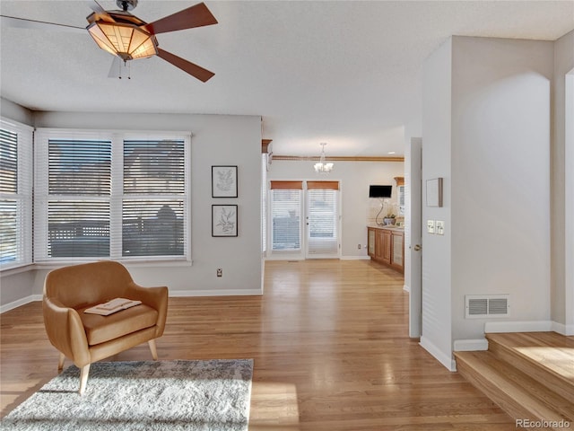 living area featuring ceiling fan with notable chandelier, a healthy amount of sunlight, light wood-type flooring, and crown molding