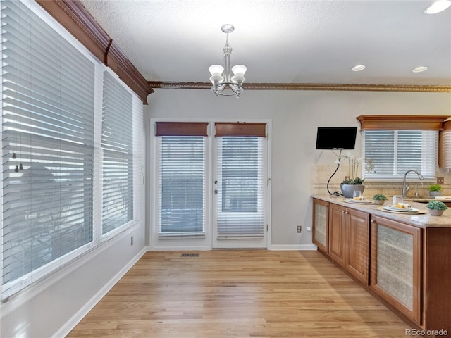 dining room with sink, light wood-type flooring, ornamental molding, a healthy amount of sunlight, and a chandelier