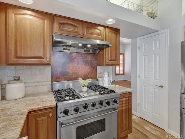 kitchen featuring decorative backsplash, light hardwood / wood-style floors, light stone countertops, and high end stainless steel range oven