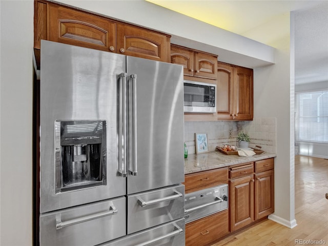 kitchen featuring backsplash, stainless steel appliances, light stone counters, and light hardwood / wood-style flooring