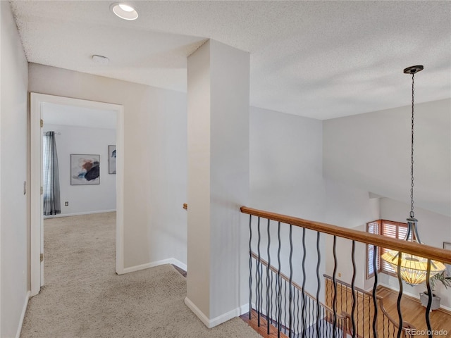 corridor with a textured ceiling and light colored carpet