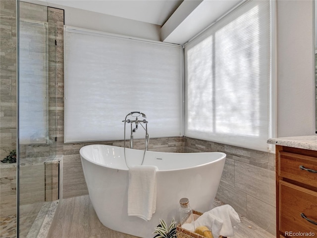 bathroom with a washtub, a wealth of natural light, tile walls, and vanity