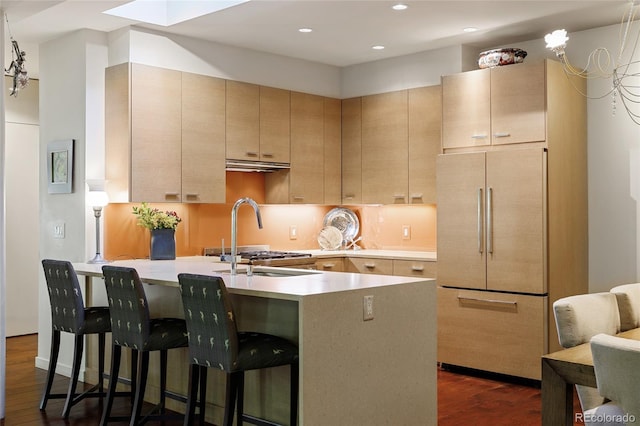 kitchen featuring a kitchen bar, a sink, fridge, light countertops, and dark wood-style flooring