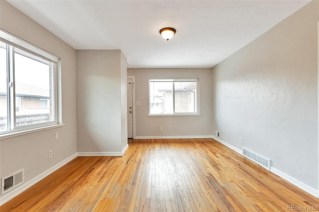 empty room with visible vents, light wood-type flooring, and baseboards