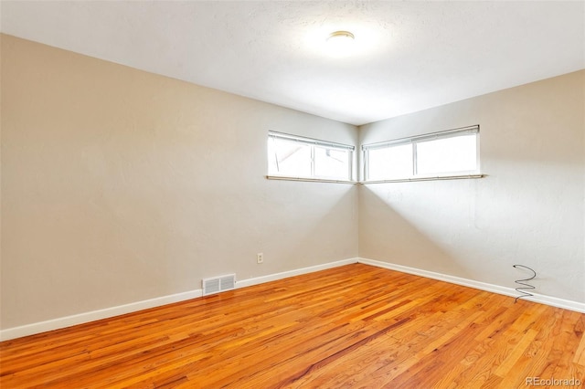 spare room featuring light wood finished floors, visible vents, and baseboards