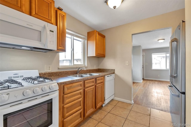 kitchen with a sink, dark countertops, white appliances, light tile patterned floors, and baseboards