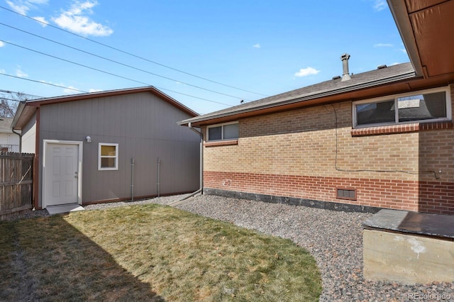 view of side of home with a yard, an outbuilding, brick siding, and fence