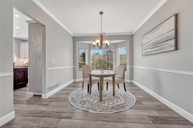 dining space featuring visible vents, baseboards, wood finished floors, crown molding, and a chandelier