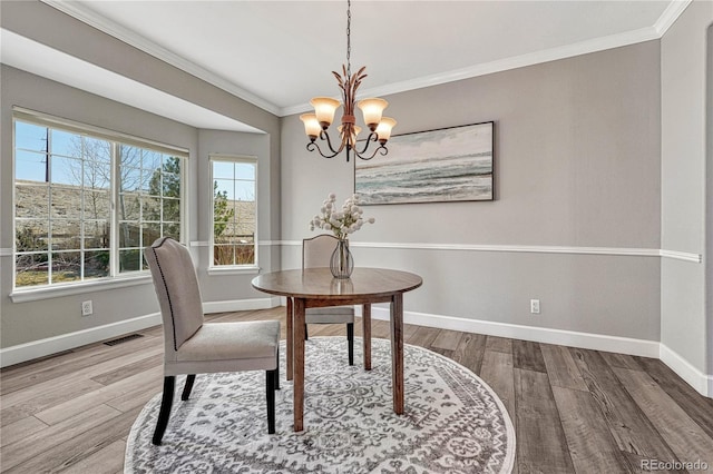 dining room with a notable chandelier, wood finished floors, visible vents, baseboards, and ornamental molding