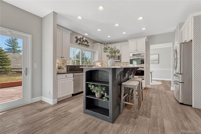 kitchen with stainless steel appliances, tasteful backsplash, light wood-type flooring, and a kitchen bar