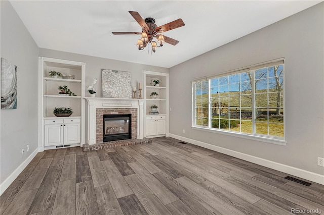 unfurnished living room with built in shelves, dark wood-style flooring, and baseboards