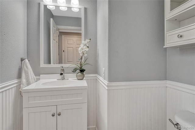 half bath with a wainscoted wall, a textured wall, and vanity