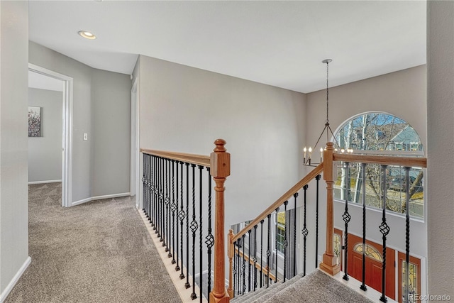 hall with a chandelier, carpet, an upstairs landing, and baseboards