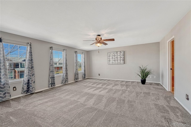 carpeted spare room featuring baseboards and a ceiling fan