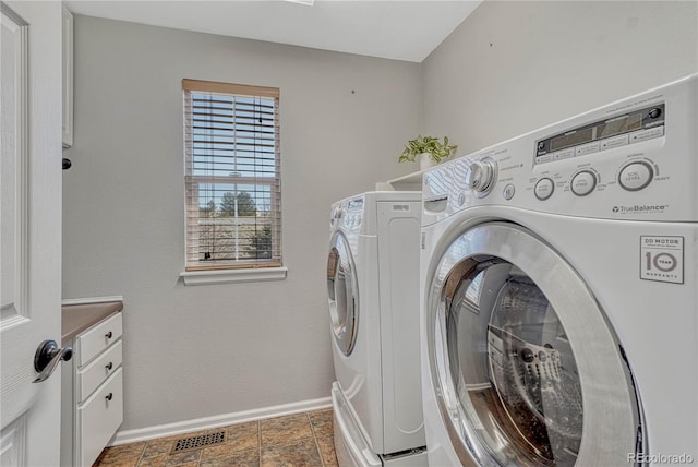 washroom featuring washer and clothes dryer, visible vents, cabinet space, stone finish floor, and baseboards