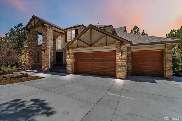 view of front facade with roof with shingles, an attached garage, driveway, and stone siding