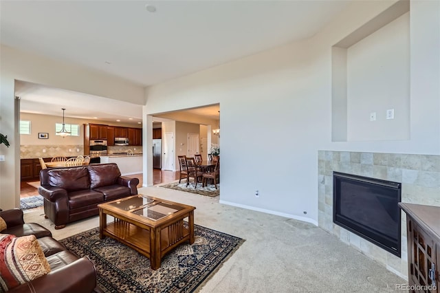 living room with light colored carpet, baseboards, a notable chandelier, and a tiled fireplace