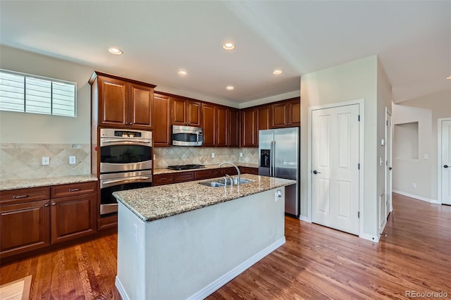 kitchen featuring a sink, light stone counters, wood finished floors, stainless steel appliances, and decorative backsplash