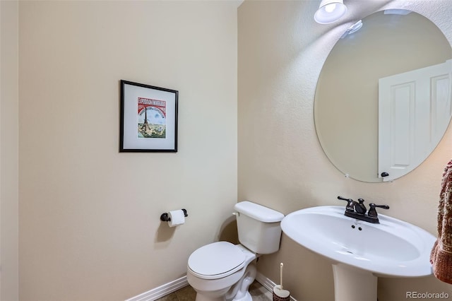 half bathroom with toilet, baseboards, and a sink