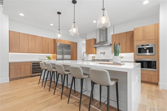 kitchen featuring wine cooler, a spacious island, built in appliances, and wall chimney range hood