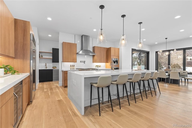 kitchen featuring a large island, pendant lighting, light hardwood / wood-style flooring, and wall chimney exhaust hood