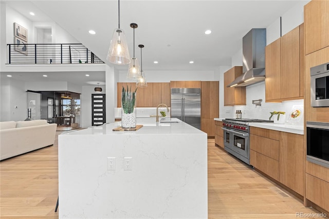 kitchen with decorative light fixtures, premium appliances, wall chimney range hood, light wood-type flooring, and a spacious island