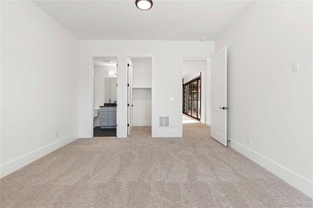 unfurnished bedroom with ensuite bath, a walk in closet, light colored carpet, and a closet