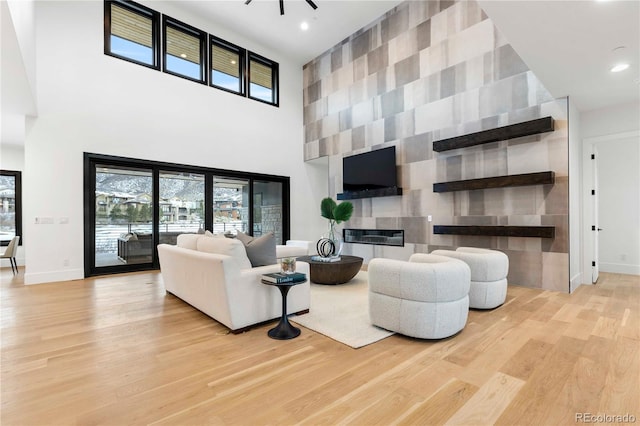 living room featuring a towering ceiling, a fireplace, and light wood-type flooring