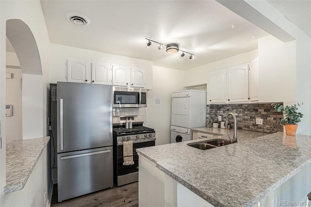 kitchen with kitchen peninsula, appliances with stainless steel finishes, sink, stacked washer / dryer, and white cabinetry