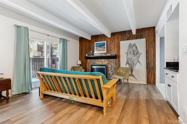 living room with light hardwood / wood-style flooring, beam ceiling, a stone fireplace, and wood walls