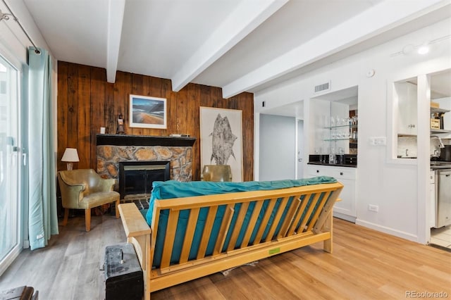 bedroom with bar, a stone fireplace, light wood-type flooring, wooden walls, and beamed ceiling