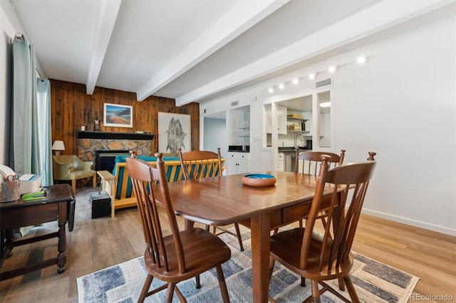 dining room with a stone fireplace, wood-type flooring, beamed ceiling, and wood walls