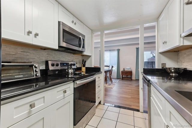 kitchen featuring light tile patterned flooring, appliances with stainless steel finishes, white cabinets, and decorative backsplash