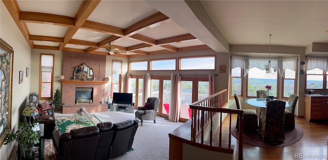 living area featuring a brick fireplace, coffered ceiling, beamed ceiling, and ceiling fan with notable chandelier