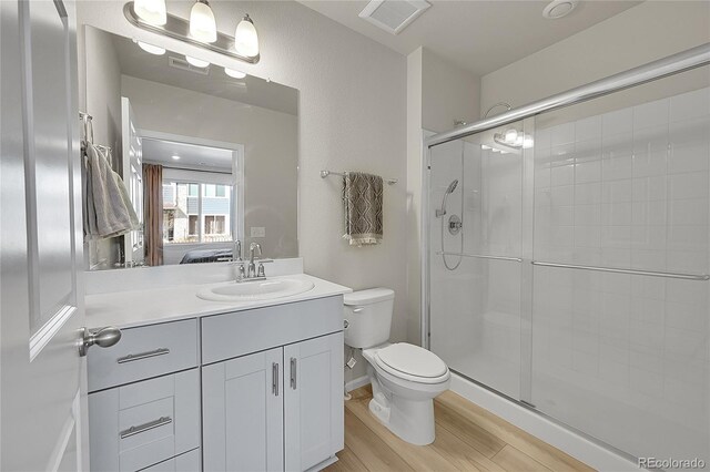 bathroom with a shower stall, wood finished floors, vanity, toilet, and visible vents