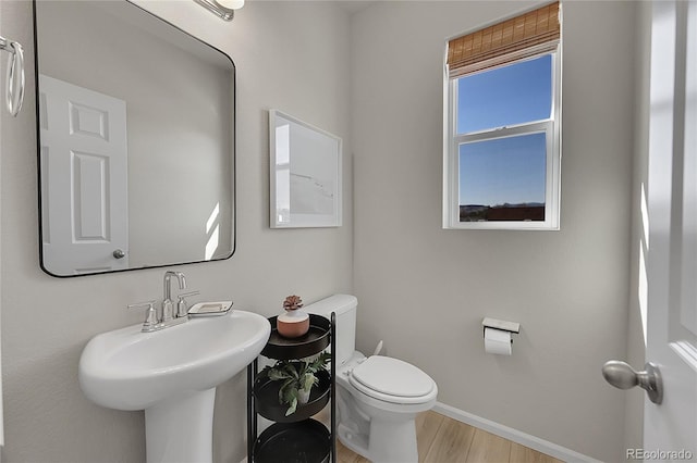 bathroom featuring baseboards, toilet, wood finished floors, and a sink