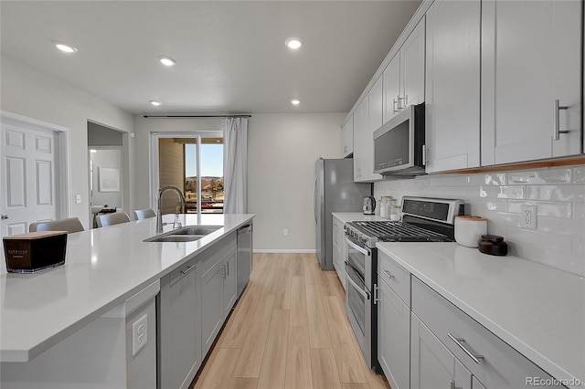 kitchen with light countertops, a sink, light wood-style flooring, tasteful backsplash, and appliances with stainless steel finishes