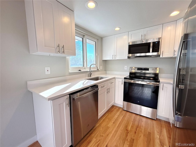 kitchen featuring white cabinets, appliances with stainless steel finishes, light wood-type flooring, and sink