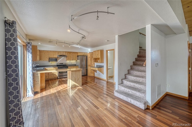 kitchen with a textured ceiling, visible vents, baseboards, stainless steel appliances, and light wood-type flooring