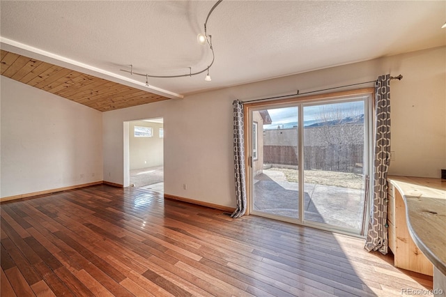 unfurnished dining area featuring hardwood / wood-style floors, baseboards, vaulted ceiling, and a textured ceiling