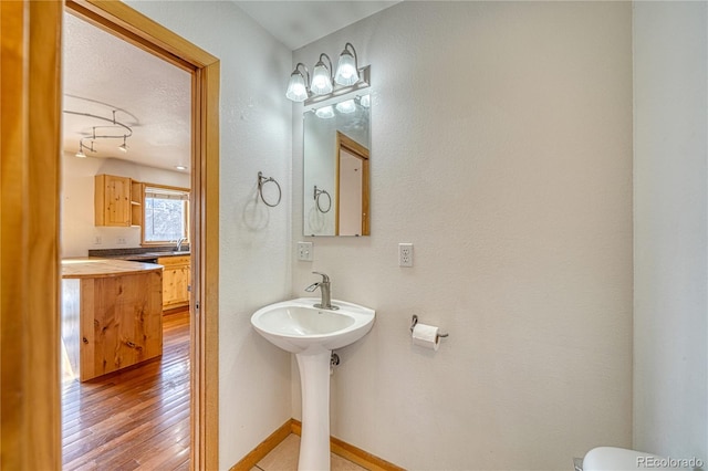 bathroom with baseboards, toilet, wood finished floors, and a sink