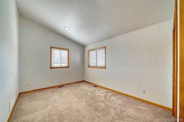 empty room with baseboards, lofted ceiling, visible vents, and light carpet