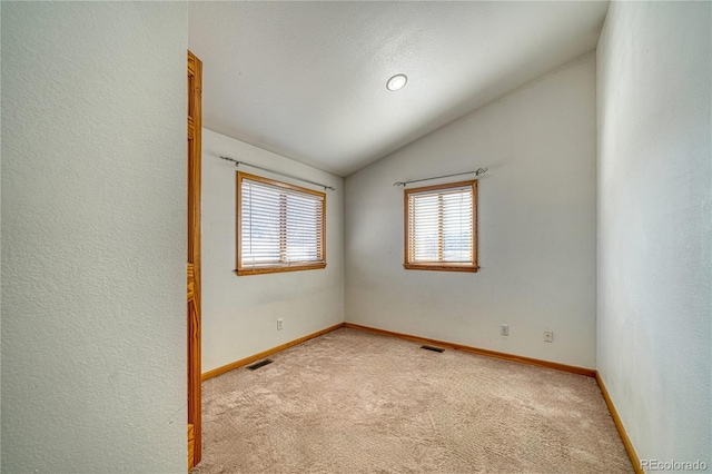 carpeted empty room featuring baseboards, lofted ceiling, and visible vents