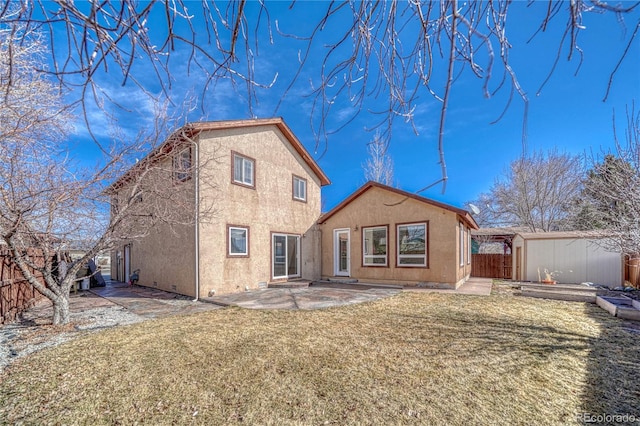 rear view of house with an outdoor structure, stucco siding, a patio, a fenced backyard, and a lawn