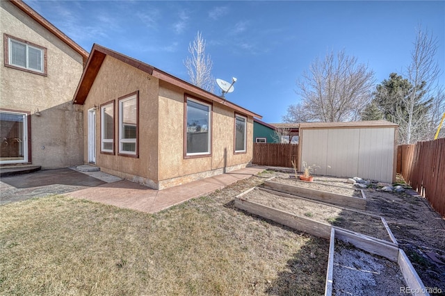 back of house featuring a fenced backyard, a vegetable garden, stucco siding, an outbuilding, and a yard