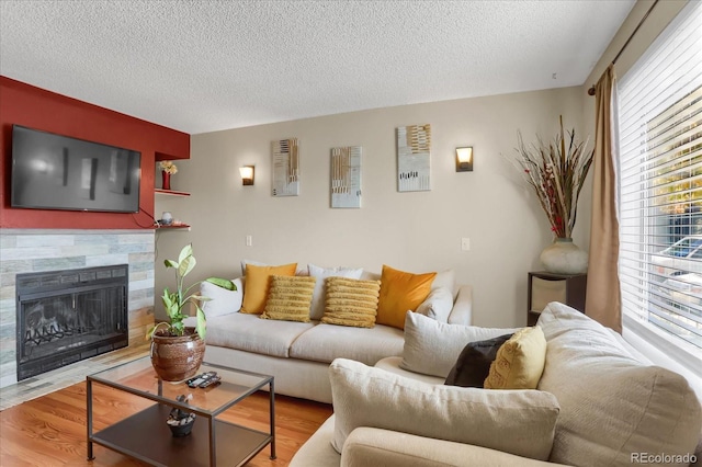 living room with a stone fireplace, a textured ceiling, and hardwood / wood-style flooring